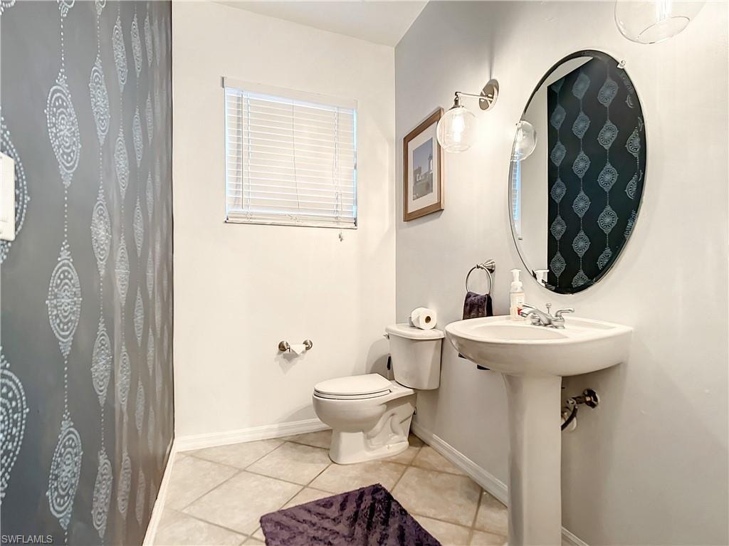 Pedestal sink with chrome faucet, oval wall-mounted mirror, and ceramic tile flooring