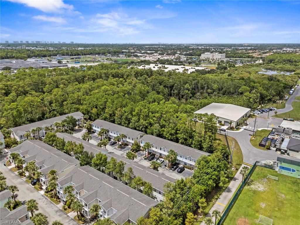 Community featuring multiple townhome-style buildings, green spaces, and adjacent wooded areas