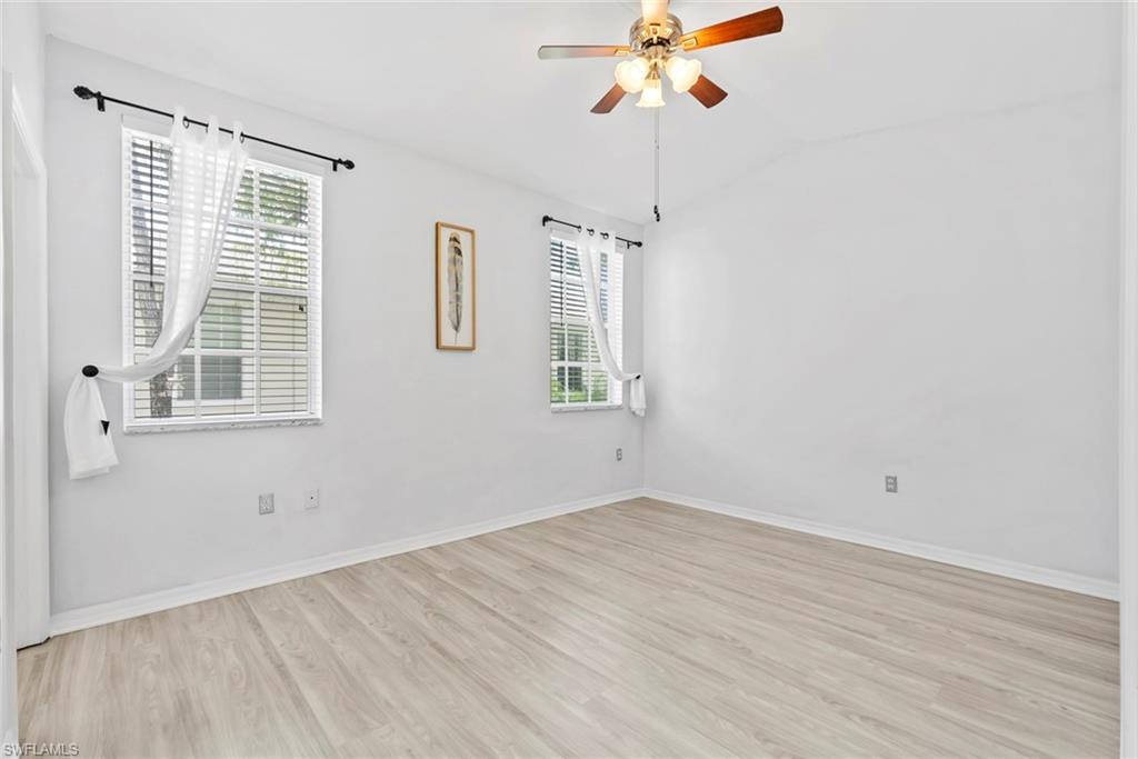 Vaulted ceiling, wood-finish flooring, two windows with blinds, ceiling fan with integrated lighting, and white walls