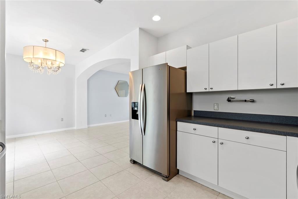 White cabinetry with dark countertops, stainless steel refrigerator, tile flooring, and an arched doorway