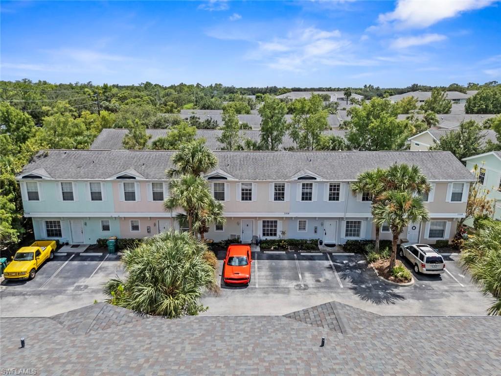 Two-story multi-family structure with dormer windows, individual parking spaces, and mature landscaping