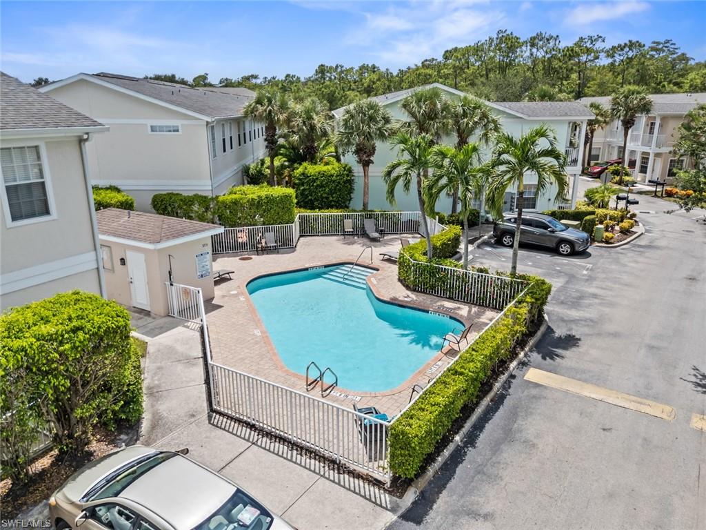 Community swimming pool featuring a brick paver deck, perimeter fencing, and surrounding palm trees
