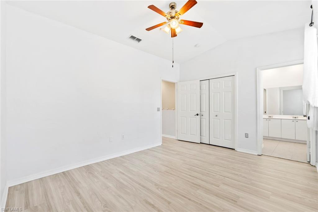 Vaulted ceiling with a ceiling fan, light wood-finish flooring, white paneled doors, and an en-suite bathroom with a double vanity