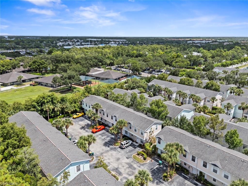 Expansive community with multiple residential buildings, abundant mature trees, paved parking areas, and a visible sports court