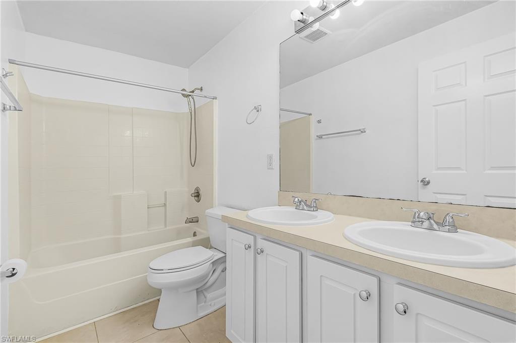 Dual vanity with integrated sinks, white cabinetry with chrome hardware, full-width mirror, and a bathtub with shower