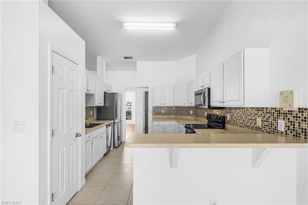 Kitchen featuring white cabinetry, stainless steel appliances, mosaic tile backsplash, and a breakfast bar