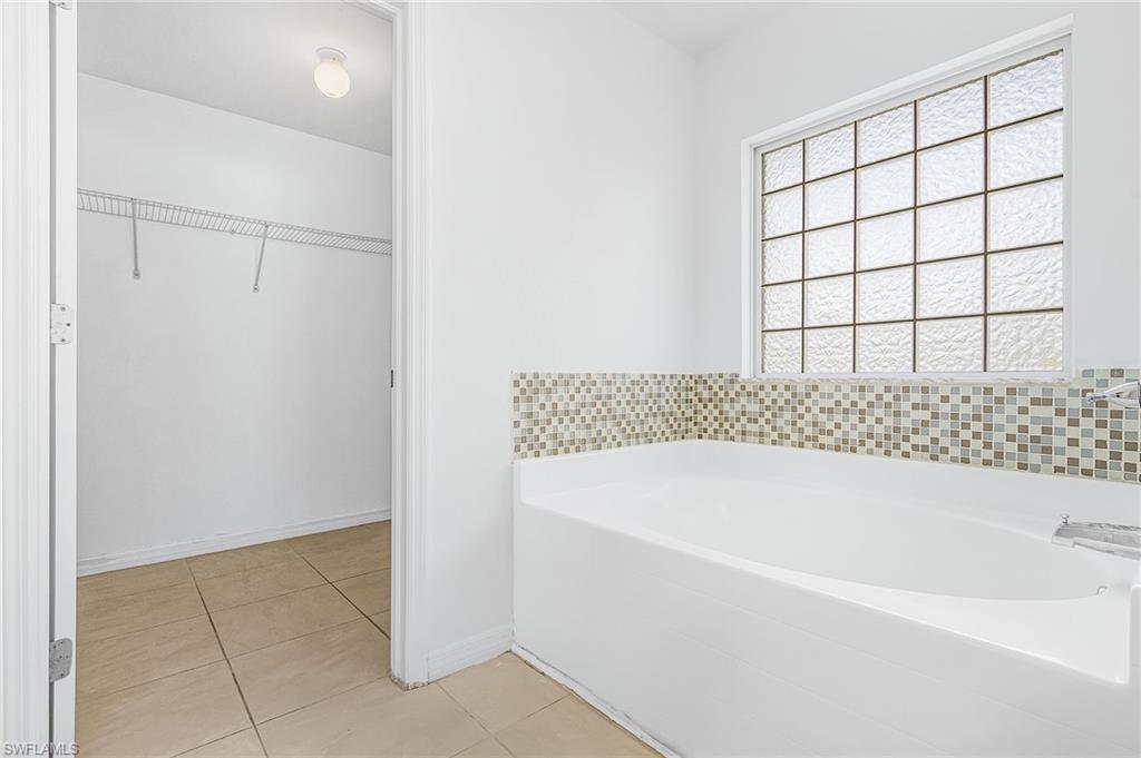 Alcove bathtub with mosaic tile surround, frosted glass window, and tile flooring