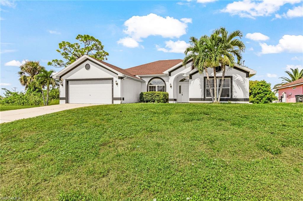 Single-story residence featuring a two-car garage, arched entry, and mature palm trees