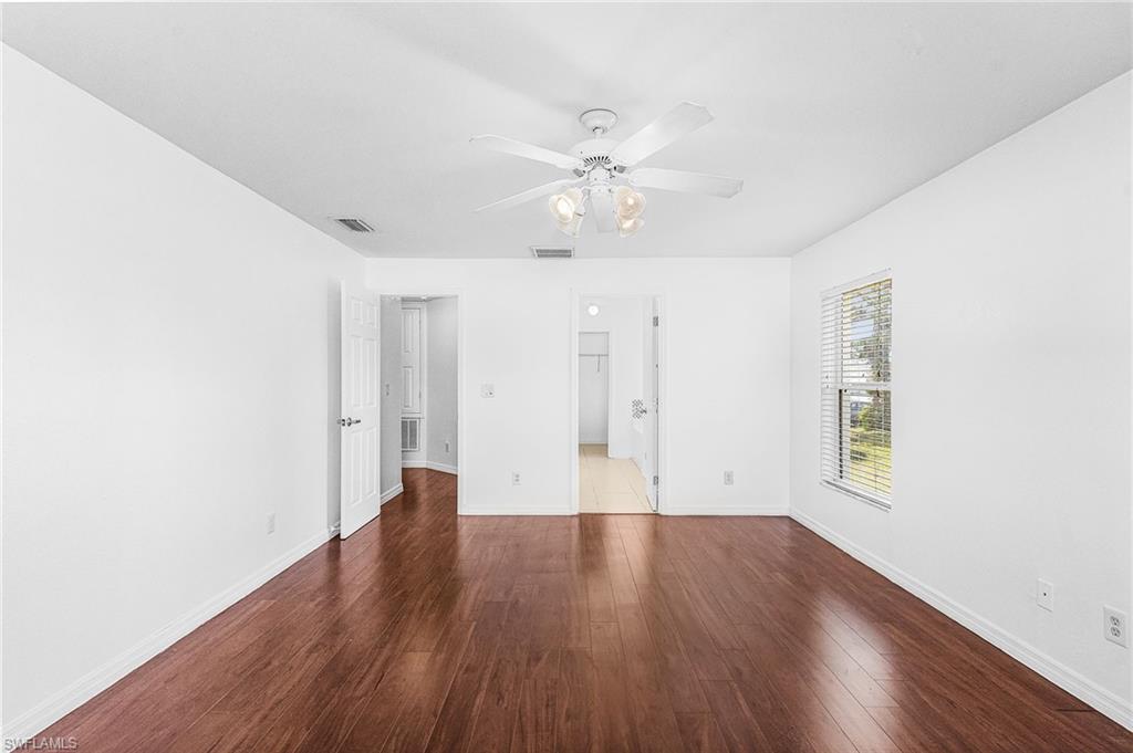 Wood-finish flooring, white walls, ceiling fan with integrated lighting, window with blinds, and white interior doors