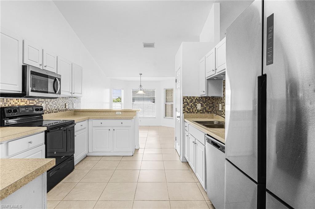 Kitchen featuring white cabinetry, tile flooring, mosaic tile backsplash, stainless steel refrigerator, and built-in microwave