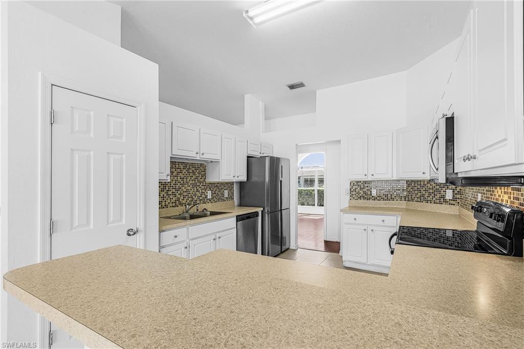 Kitchen featuring white cabinetry, light-toned countertops, a mosaic tile backsplash, and stainless steel appliances