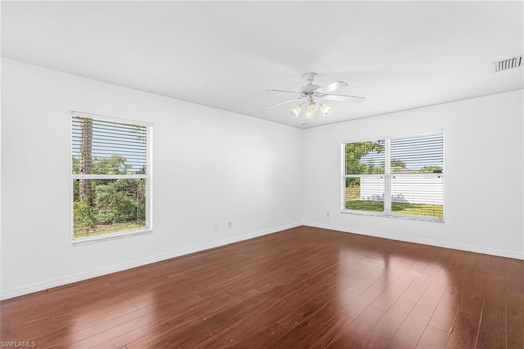 Expansive room featuring wood-finish flooring, two windows with blinds, and a ceiling fan with integrated lighting