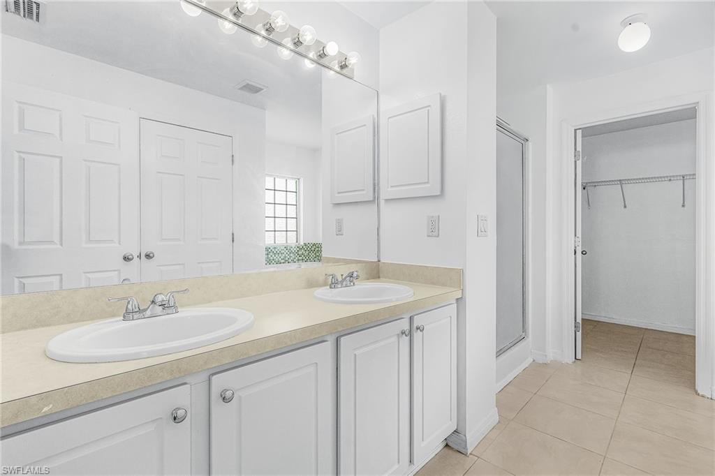 Dual vanity with white cabinetry, a large mirror, and overhead lighting