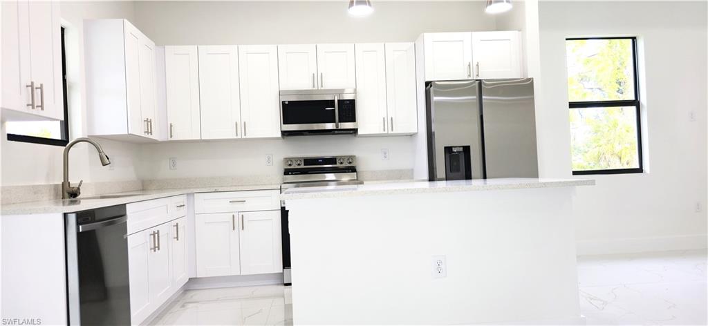 Kitchen featuring white cabinetry, light-toned countertops, stainless steel appliances, and a central island