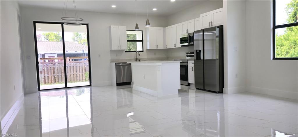 Polished tile flooring, white shaker cabinetry, stainless steel appliances, kitchen island, and sliding glass doors