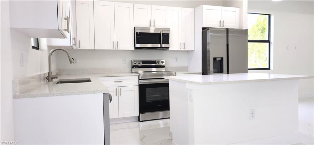 Contemporary kitchen featuring white shaker cabinetry, stainless steel appliances, light-toned countertops, and a kitchen island with seating