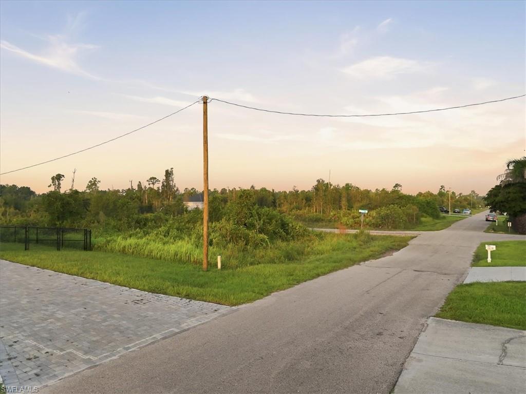 Paved road frontage, mature landscaping, and an adjacent paved patio area