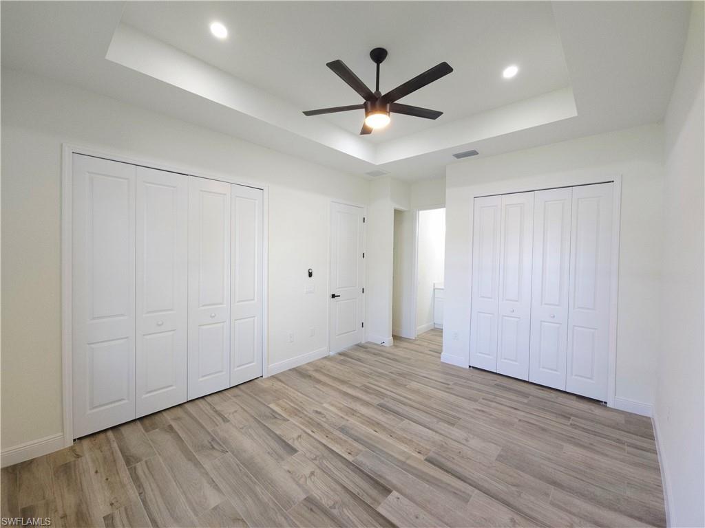 Tray ceiling with recessed lighting and a ceiling fan, wood-finish flooring, and white bifold closet doors