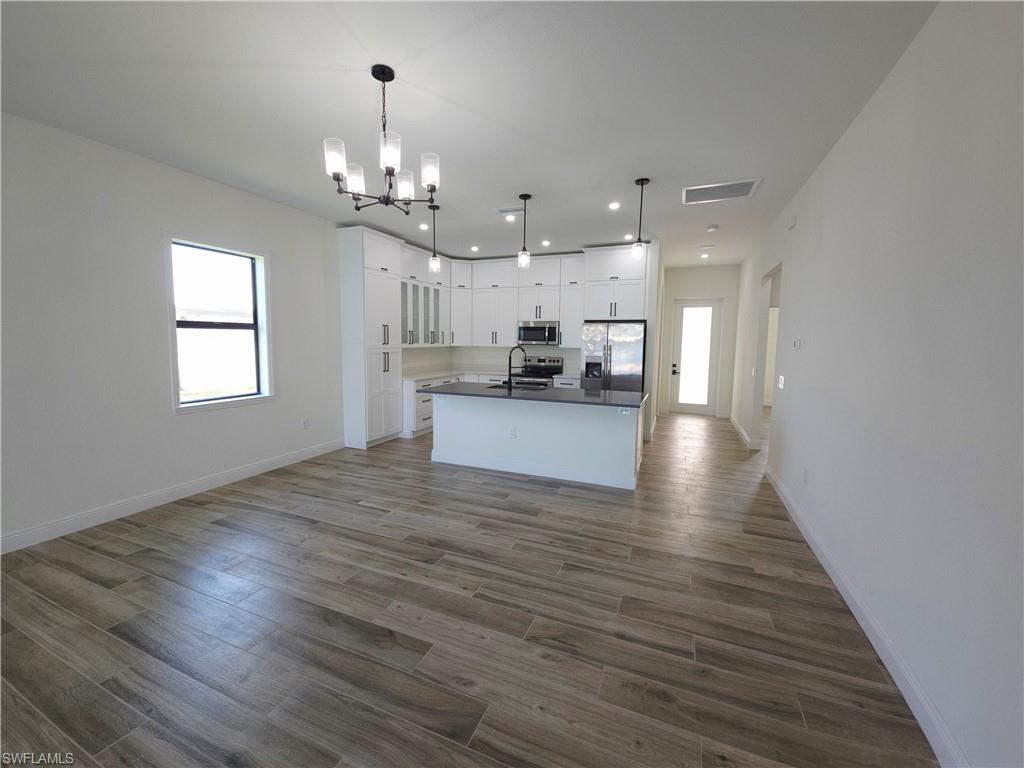 Open-concept living space with wood-finish flooring, white cabinetry, dark countertops, and stainless steel appliances