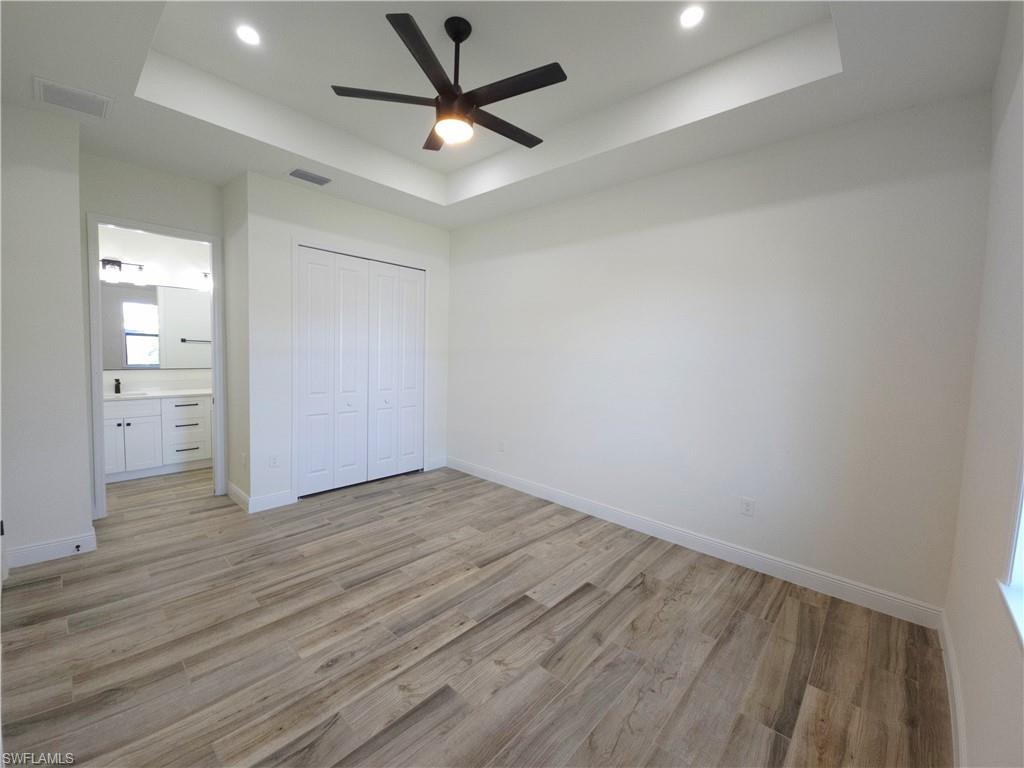 Tray ceiling with recessed lighting and a ceiling fan, wood-finish flooring, bi-fold closet doors, and an attached bathroom with a vanity