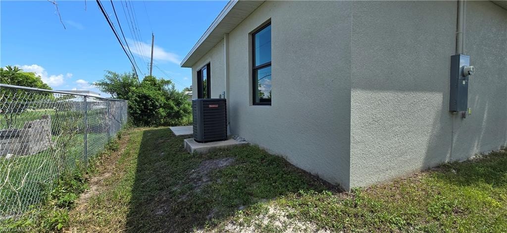 Stucco exterior with black-framed windows, an outdoor HVAC unit on a concrete pad, and a chain-link fence