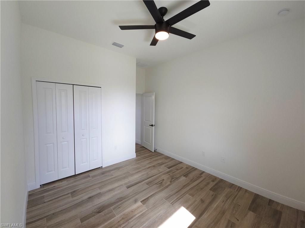Bedroom 3, Wood-finish flooring, white bi-fold closet doors, white walls, and a ceiling fan with integrated lighting