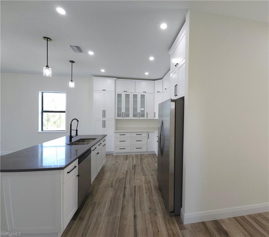 Kitchen featuring wood-finish flooring, white cabinetry, a black countertop, and stainless steel appliances