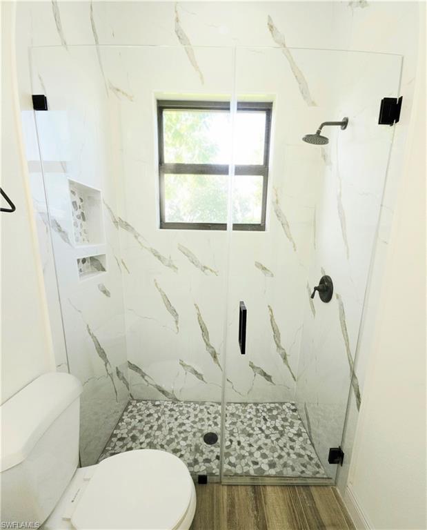 Frameless glass shower enclosure with a rainfall shower head, pebble-tile flooring, and built-in shelving