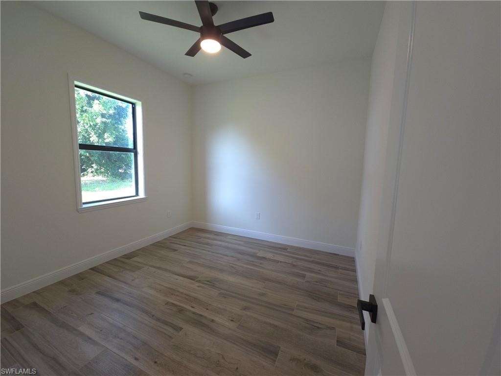 Bedroom 2, Neutral wall color, wood-finish flooring, ceiling fan, single window, and white trim