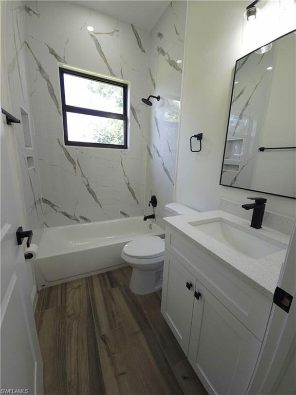 Bathroom featuring a white vanity with a light-colored countertop, wood-finish flooring, and a shower/tub combination with white and grey patterned wall tiles