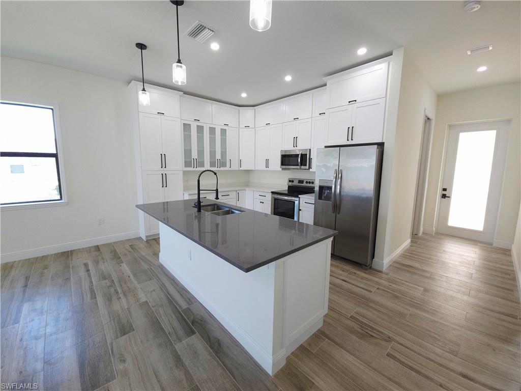 Modern kitchen featuring white cabinetry, a large island with a dark countertop, stainless steel appliances, and wood-finish flooring
