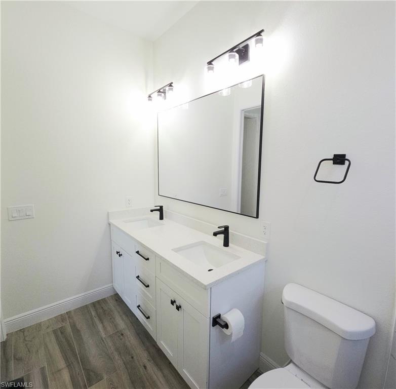 Dual vanity with white cabinetry and matte black hardware, white countertop, rectangular framed mirror, and wood-finish flooring