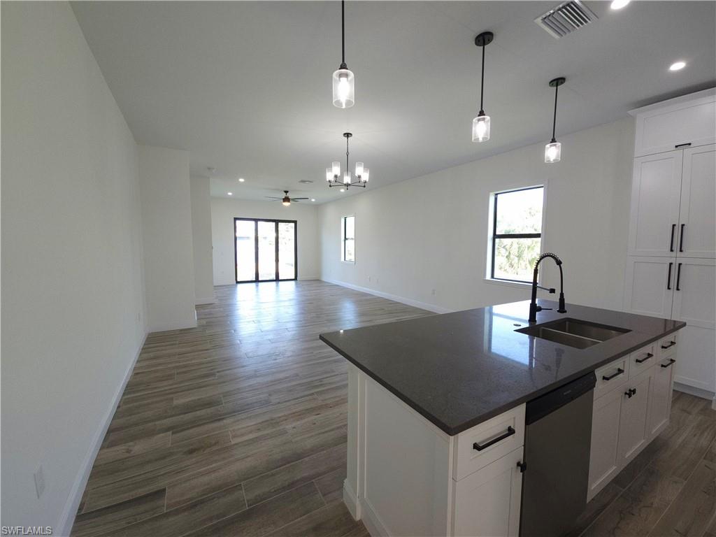 Spacious open-concept interior featuring wood-finish flooring, a kitchen island with a dark countertop and undermount sink, white cabinetry with dark hardware, and pendant lighting