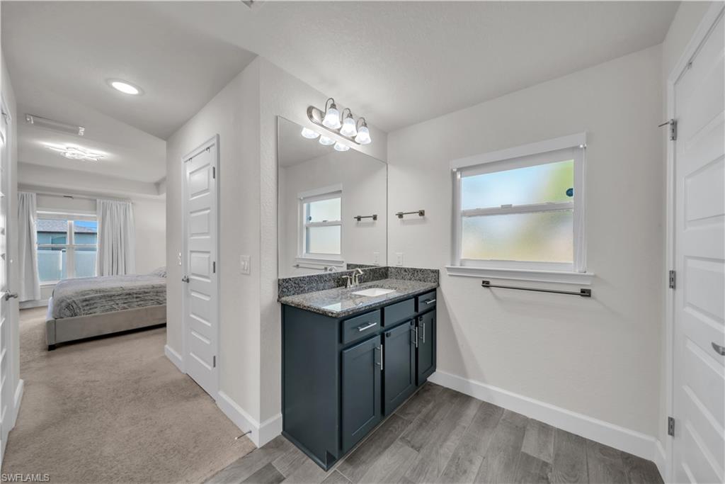 Floating vanity with a stone countertop and integrated sink, framed mirror, and wood-finish flooring