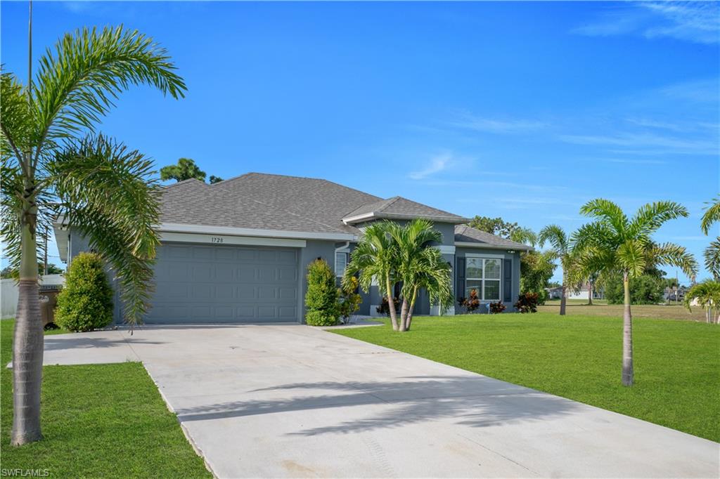 Single-story residence with a two-car garage, concrete driveway, and a front lawn with established palm trees and shrubs