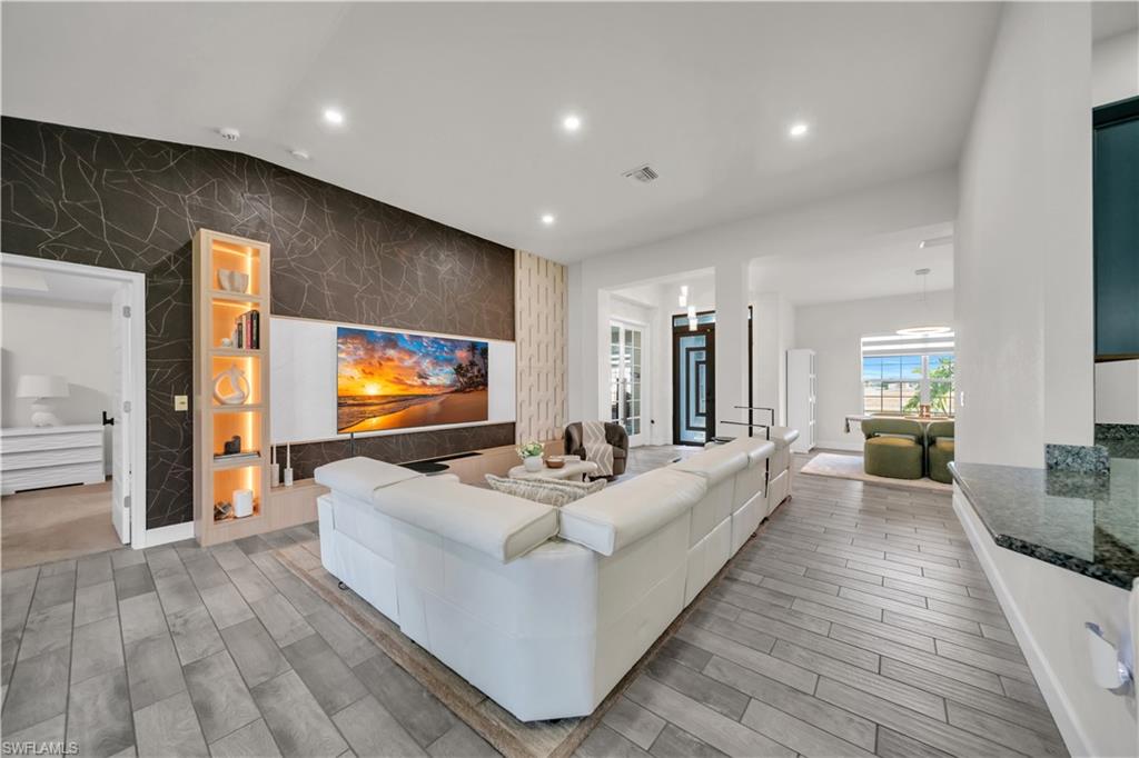 Vaulted ceiling, recessed lighting, wood-finish flooring, built-in display shelving with accent lighting, and a stone countertop