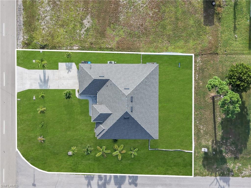 Gable roof with dark gray shingles, concrete driveway, lush green lawn, and mature palm trees