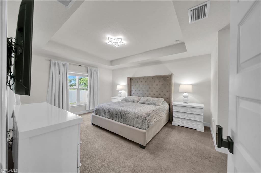 White walls, tray ceiling with recessed lighting, wall-mounted television, and carpeted flooring
