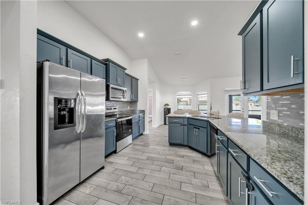 Kitchen featuring stainless steel appliances, granite countertops, blue cabinetry, tile flooring, and recessed lighting