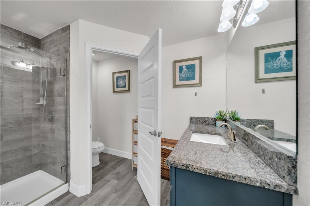 Glass-enclosed shower with subway tile surround, granite countertop vanity with integrated sink, and wood-finish flooring