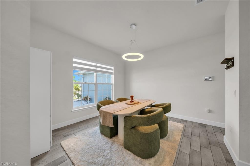 Light-filled dining space featuring a window with horizontal blinds, wood-finish flooring, and a modern circular pendant light