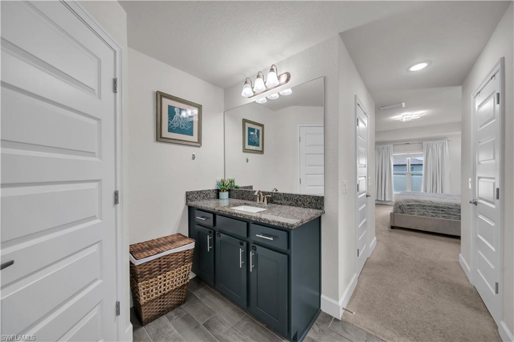 Vanity with dark cabinetry and a stone-finish countertop, undermount sink, and wall-mounted mirror