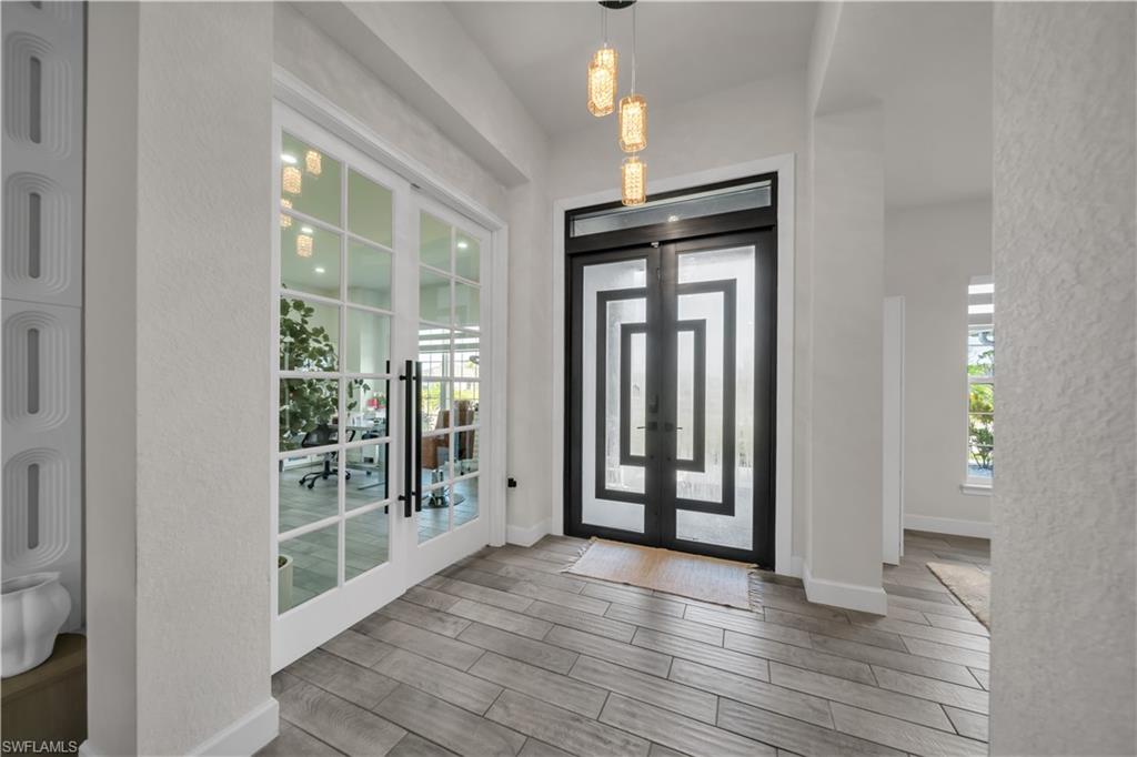 Foyer featuring wood-finish tile flooring, a modern multi-pendant light fixture, and a frosted glass double entry door with geometric detailing