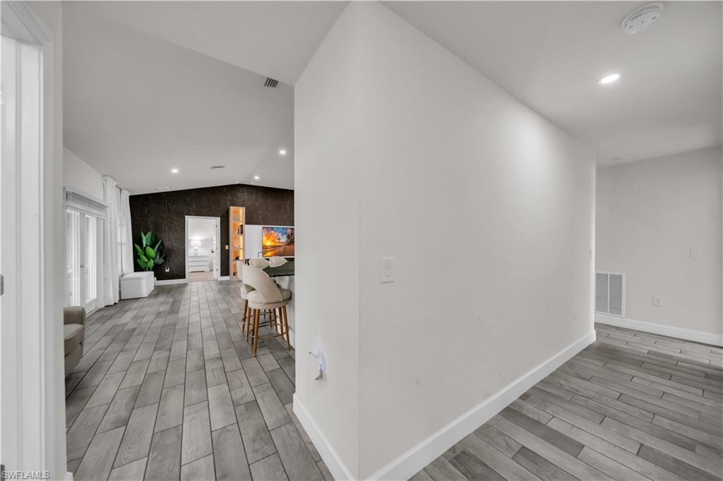 Vaulted ceiling, recessed lighting, wood-finish flooring, two-panel interior doors, and a dark accent wall