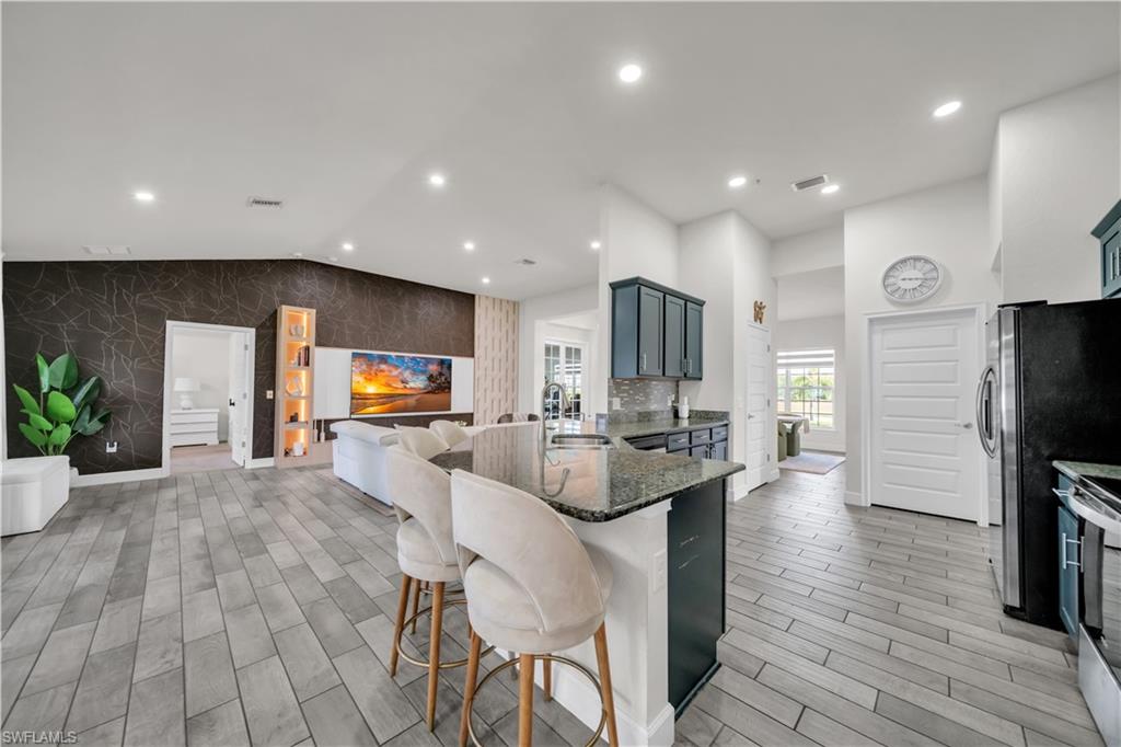 Spacious open-concept living area featuring wood-finish flooring, a kitchen island with seating, dark cabinetry, and recessed lighting
