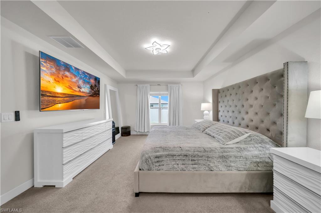 Tray ceiling with central light fixture, carpeted flooring, and window with vertical blinds