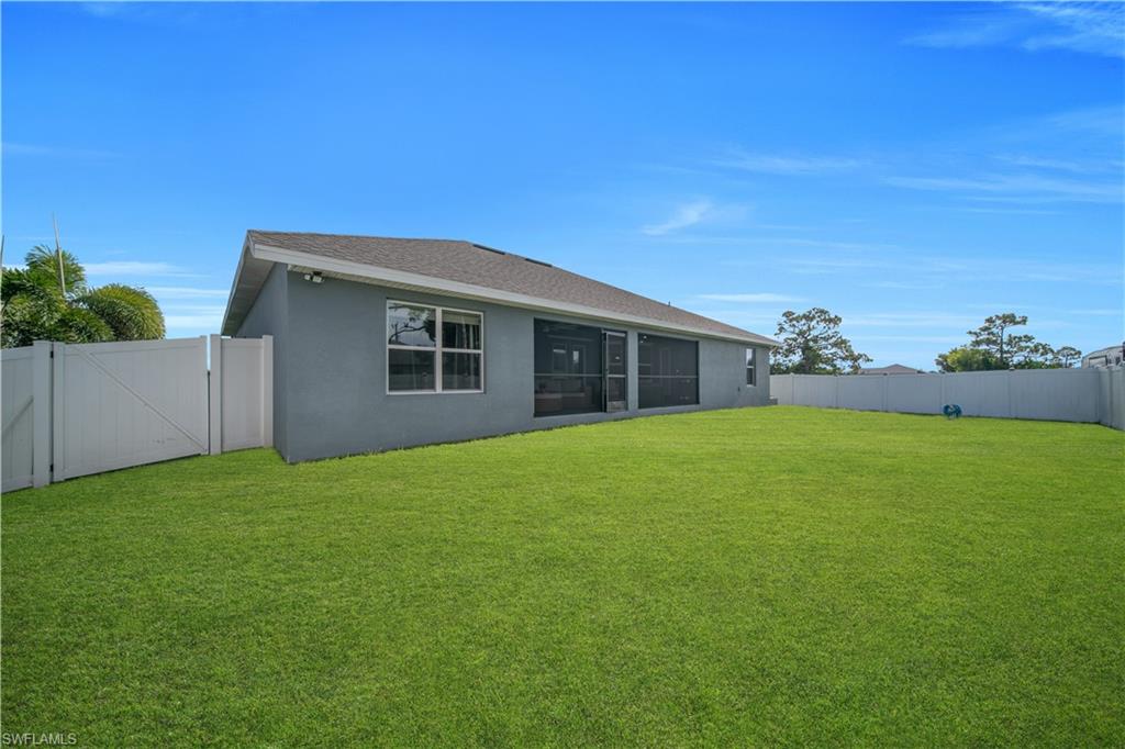 Expansive backyard featuring a manicured lawn, full privacy fencing, and a screened-in patio with sliding glass doors