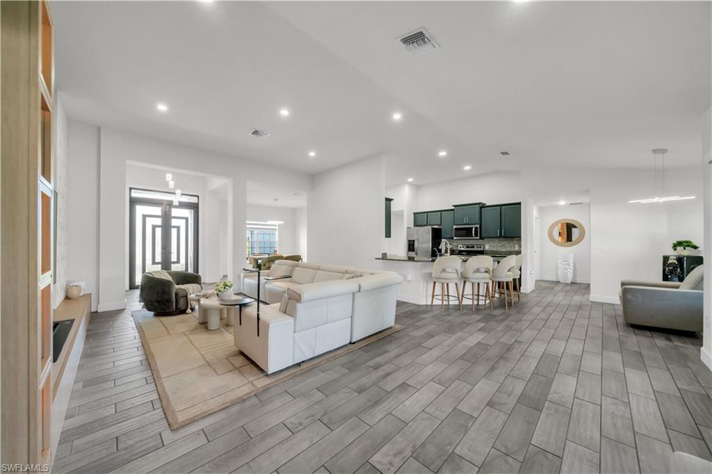 Open-concept living space featuring wood-finish flooring, recessed lighting, a kitchen island with seating, and dark-finished cabinetry