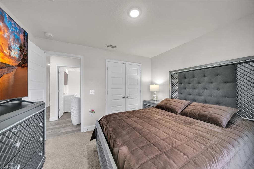 Recessed lighting illuminates the room, featuring light gray walls, a carpeted floor, and a double-door closet