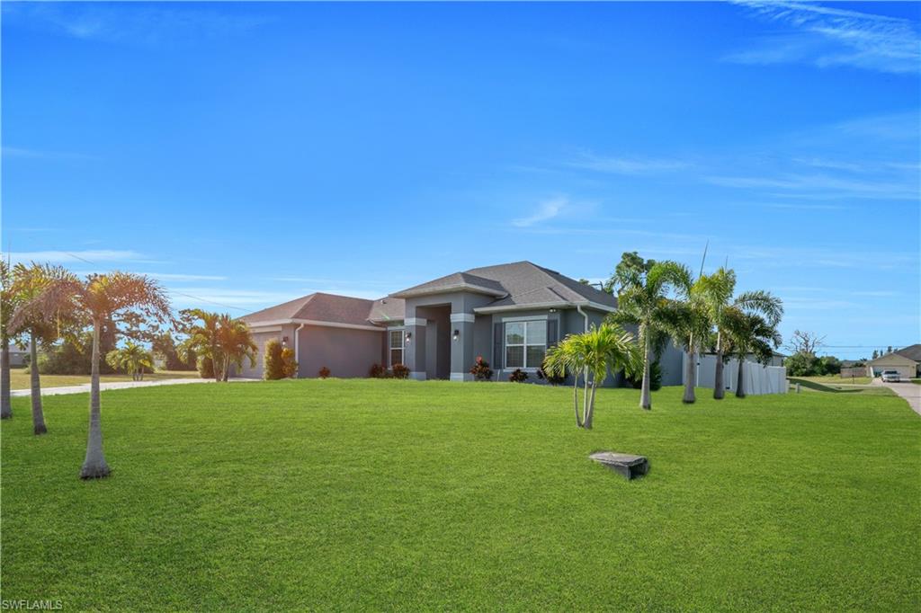 Expansive front yard with a lush green lawn, mature palm trees, and a concrete driveway